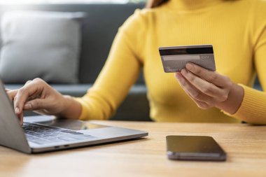 Kadının elinde dizüstü bilgisayarla kredi kartı tutuyor ve güvenlik kodunu not defteri klavyesi, online teknoloji alışverişi, kredi kartı ödemesi kullanarak giriyor.