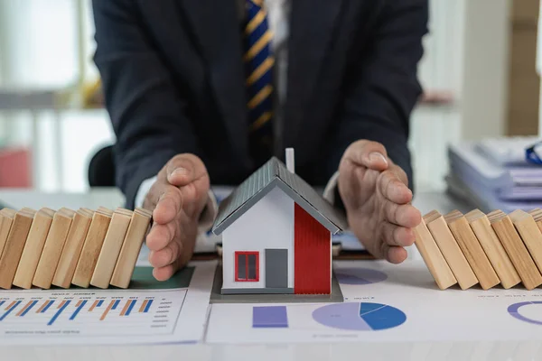 Real Estate Protection Risk Business Plan Human hands protect a row of falling wooden blocks like dominoes to a house model. Insurance concept to protect against property loss Close-up pictures