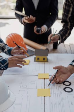 İnşaat şantiyesi mühendisleri kağıt sayfaları üzerindeki planları inceliyor ve şantiyede bir bina inşa etmek için birlikte çalışmayı planlıyorlar. dikey resim