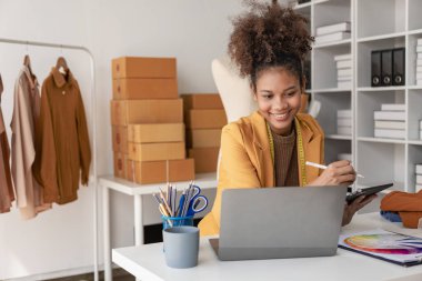 Canlı yayın videosunda kıyafet satan genç Afrikalı kadın isim siparişleri almak ve paket göndermeye hazır olmak için akıllı telefon ya da tabletinizi kullanarak küçük bir KOBİ başlatın.