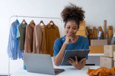 Canlı yayın videosunda kıyafet satan genç Afrikalı kadın isim siparişleri almak ve paket göndermeye hazır olmak için akıllı telefon ya da tabletinizi kullanarak küçük bir KOBİ başlatın.