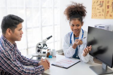 Genç Asyalı adam hastanede Afrikalı kadın doktorla hastalıkları tartışıyor, sağlık konsepti