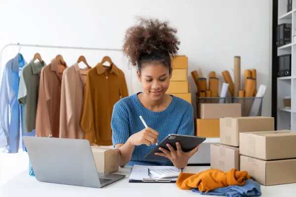 Young African woman selling clothes in streaming video Start a small SME using your smartphone or tablet to receive name orders and ready to ship packages.