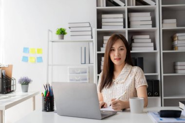 Vergi hesaplama tablosu raporları, şirket mali istatistikleri ve analitik araştırma fikirleri için hesap makinesi ve dizüstü bilgisayar kullanan Asyalı kadın çalışanlar