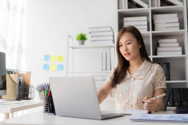 Vergi hesaplama tablosu raporları, şirket mali istatistikleri ve analitik araştırma fikirleri için hesap makinesi ve dizüstü bilgisayar kullanan Asyalı kadın çalışanlar