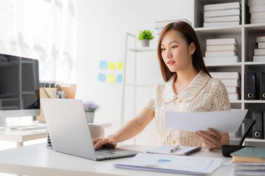 Vergi hesaplama tablosu raporları, şirket mali istatistikleri ve analitik araştırma fikirleri için hesap makinesi ve dizüstü bilgisayar kullanan Asyalı kadın çalışanlar