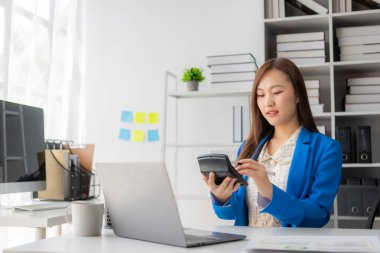 Vergi hesaplama tablosu raporları, şirket mali istatistikleri ve analitik araştırma fikirleri için hesap makinesi ve dizüstü bilgisayar kullanan Asyalı kadın çalışanlar