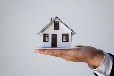 Takım elbiseli bir işadamı ev modelini avucunun içinde tutuyor. Konut kredisi Konsepti Emlak Sigortası
