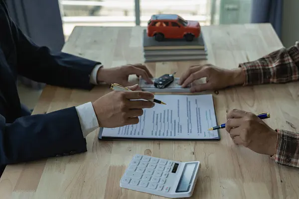 Car rental service concept The agent gives the car keys to the customer after signing the rental contract, car insurance document or paper contract of agreement for the purchase or sale of a new car.