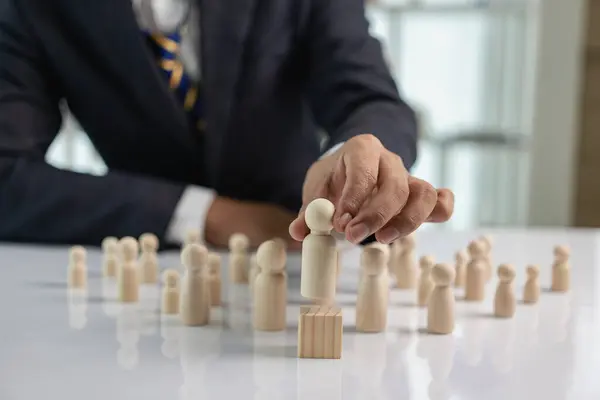 Businessman holding a wooden figure in front of him, leadership concept, collection of wooden figures, common figure to represent conformity and crowd.