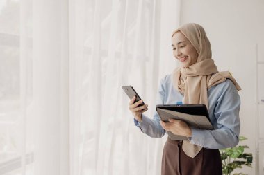 Güzel Asyalı Müslüman iş kadını sosyal medya uygulamasını görmek için akıllı telefon kullanıyor. Müşterilerle sohbet ediyor ya da ticari işlemleri tartışıyor..