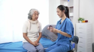 Asyalı hemşire hastane yatağında yaşlı Asyalı kadın hastayı kontrol ediyor. Çekici bakıcı, klinik 44k 60p 'de yaşlı büyükannesine danışmanlık ve danışmanlık yapar.