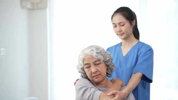 女性医師のヘルスケアコンセプトで痛みを伴う腕をリハビリするために女性患者の負傷した腕の治療を検討する高齢のアジアの女性に物理療法を行う理学療法士 — ストック動画