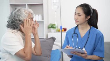 Asyalı hemşire hastane yatağında yaşlı Asyalı kadın hastayı kontrol ediyor. Çekici bakıcı, klinik 44k 60p 'de yaşlı büyükannesine danışmanlık ve danışmanlık yapar.
