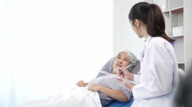 Asyalı hemşire hastane yatağında yaşlı Asyalı kadın hastayı kontrol ediyor. Çekici bakıcı, klinik 44k 60p 'de yaşlı büyükannesine danışmanlık ve danışmanlık yapar.