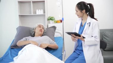 Asyalı hemşire hastane yatağında yaşlı Asyalı kadın hastayı kontrol ediyor. Çekici bakıcı, klinik 44k 60p 'de yaşlı büyükannesine danışmanlık ve danışmanlık yapar.