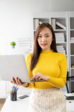 Finans ve muhasebe belgeleri üzerinde çalışan Asyalı çekici bir iş kadını ofis masasında dizüstü bilgisayarla çalışıyor. Not alıyorum. Finansal muhasebe konsepti raporu. Dikey.