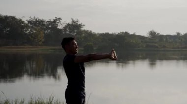 Yüksek Kaliteli 4K Genç Asyalı, yeşil parkta güneş doğarken sabah esneme egzersizi yapıyor. Sağlıklı bir yaşam tarzı ve açık hava hayatı için fikirler.