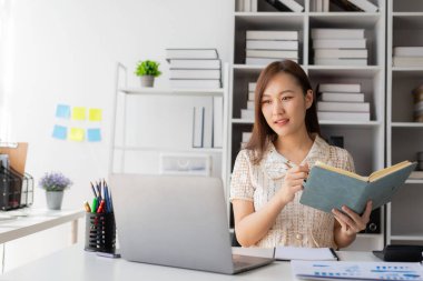 Genç Asyalı kadın bir masada oturuyor ve yatırım sonuçlarını gösteren finansal grafikleri hesaplıyor. İş büyüme sürecinizi hesap makinesi ve dizüstü bilgisayar kullanarak finansal inceleme ve bütçe ile planlayın.