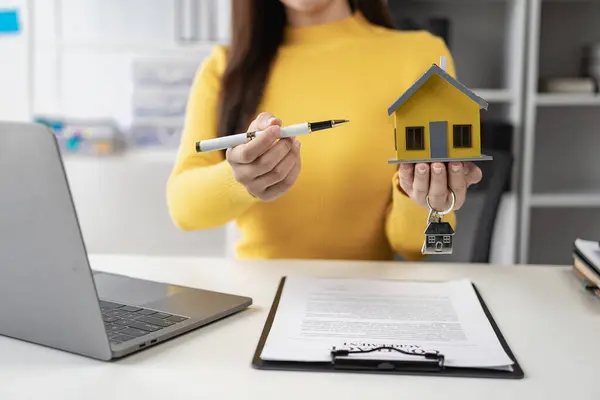 Real estate agent, young woman holding house and house keys, selling or renting property, moving house or renting property, small house, property insurance and real estate concept in office