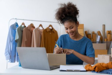 Başlangıç, küçük işletmeler, akıllı telefon ya da dizüstü bilgisayar kullanan Afrikalı kadın işletme sahibi paketlenmiş ürünleri hazırlamak için online siparişler alıyor ve onaylıyor. KOBİ iş kavramı