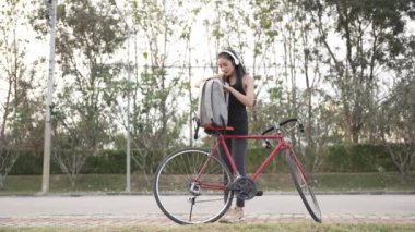 Asyalı kadın sırtında sırt çantasıyla parkta egzersiz yapmak için bisiklete biniyor. 4K video
