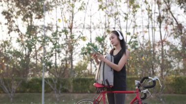 Asyalı kadın sırtında sırt çantasıyla parkta egzersiz yapmak için bisiklete biniyor. 4K video