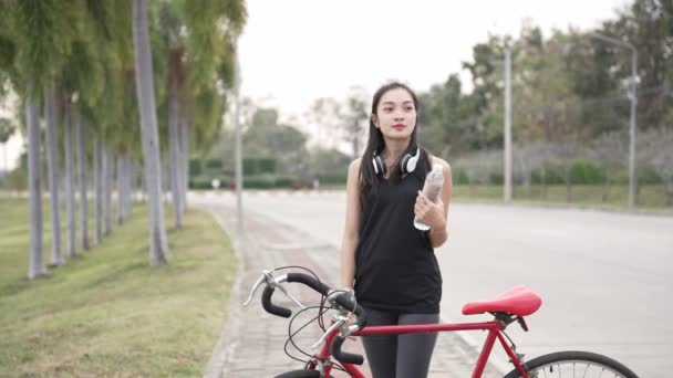 アジアの女性は 彼女の背中のバックパックで公園で運動するために喜んで自転車に乗ります 4Kビデオ — ストック動画