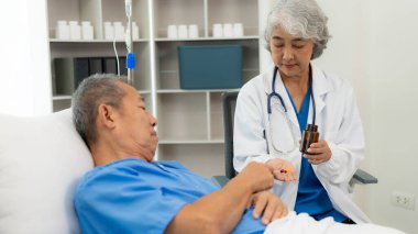 Kıdemli Asyalı kadın hemşire bir hastanın yatağında oturan, bir hastaya açıklama yapan, onunla konuşan, ilaç yazmasına yardım eden, sağlık ocağı, tıbbi danışman konseptini ziyaret ediyor.