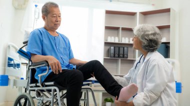 Yaşlı bir Asyalı adam yaşlı bir kadın hemşirenin desteğiyle hasta için halter ve tüpler kullanarak fizik tedavi uyguluyor..