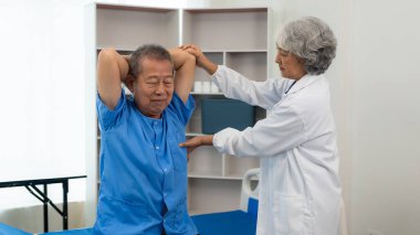 Yaşlı bir Asyalı adam yaşlı bir kadın hemşirenin desteğiyle hasta için halter ve tüpler kullanarak fizik tedavi uyguluyor..