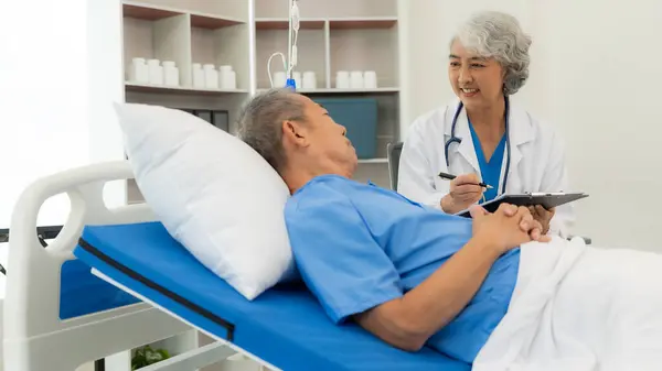 Senior Asian female nurse doctor visits a senior patient sitting on a patient\'s bed, explaining, talking to a patient, helping prescribe medication, health care clinic, medical consultant concept