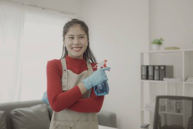 Asyalı kadın ev işi yapıyor önlük takıyor oturma odasının ahşap zeminini temizliyor Mutlu ev kadını evde ev işi yapıyor çekici bir gülümsemeyle, ev temizliği konseptiyle