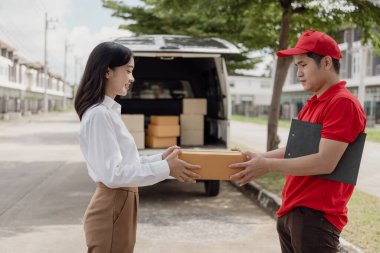 Genç Asyalı kadın, mutlu ve gülümseyen postacıdan bir karton kutu alır. Kurye, öğeyi acilen teslim eder. Çevrimiçi mağaza, kağıt konteynırlar, postacı, teslimat servisi, paketler