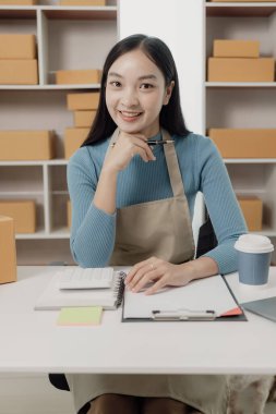 Posta paketi. Çevrimiçi satış. KOBİ başlangıç konsepti. Bağımsız Asyalı kadın küçük işletme girişimcisi. Önlük takıyor. İnternetten yemek sipariş etmek için laptop ve kutu kullanıyor. KME iş dikey resmi