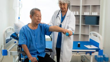 Yaşlı bir Asyalı adam oturma odasında yaşlı bir kadın hemşirenin desteğiyle fizik tedavi uyguluyor..