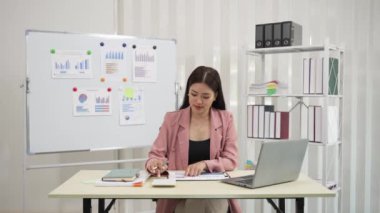 Finansal grafik belgeleriyle çalışan ve birikimleri hesaplamak için hesap makinesi kullanan genç Asyalı muhasebeci veya dizüstü bilgisayar ve vergi kopyalama, ticaret, araştırma, muhasebe belgesi, şirket 4k