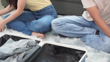 Asyalı bir çift, yurtdışı seyahati için kıyafetlerini oturma odasının zemininde bavullara doldurup tatil için hazırlanıyorlar..