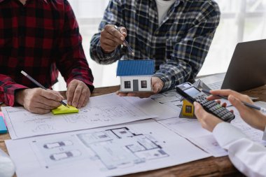 İnşaat mühendisi ve ustabaşı inşaat alanı planlaması hakkında tartışıyorlar ve teknik yönleri tartışmak üzere iç mimari yapı taslağının planlarına işaret ediyorlar..