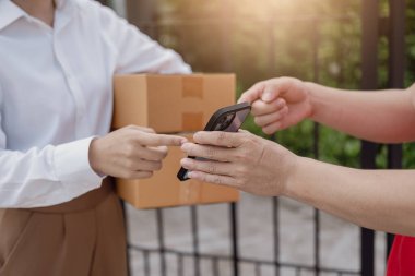 Lojistik konsepti A paketi ya da teslimat servisi çevrimiçi alışveriş, nakliye ya da e-ticaret için bir hizmet sağlayıcısının ya da ürünün kapısında duruyor. - Cep telefonuyla ödeme yaparken yakın plan görüntüsü