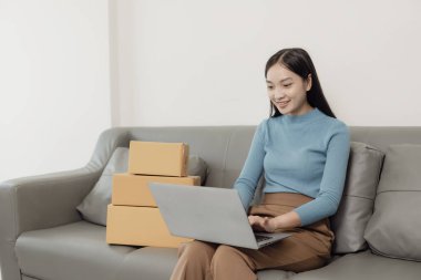 KOBİ 'li kadın girişimci, müşterilere satacak kutular hazırlamak için fatura kutuları ve online siparişleri kontrol ediyor. KOBİ iş konsepti, çevrimiçi sipariş, ürünleri satmak, kutularla çalışmak, serbest çalışmak.