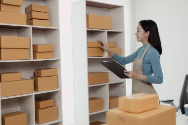 KOBİ 'li kadın girişimci, müşterilere satacak kutular hazırlamak için fatura kutuları ve online siparişleri kontrol ediyor. KOBİ iş konsepti, çevrimiçi sipariş, ürünleri satmak, kutularla çalışmak, serbest çalışmak.