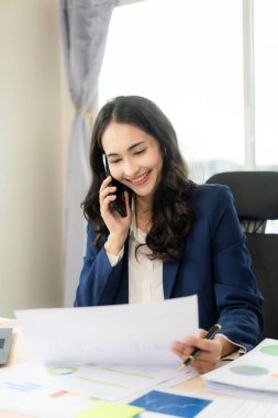 Belgeler ve dizüstü bilgisayarla çalışan Asyalı iş kadını işçi belgeleri, mali göstergeleri hesaplıyor, gülümsüyor ve işin başarısından memnun..
