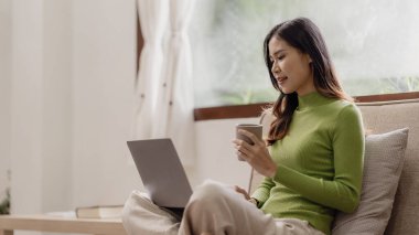 İnternette dizüstü bilgisayarda çalışan Asyalı bir kız evdeki kanepede oturup internetten alışveriş yapıyor.