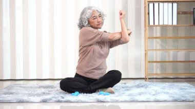 Spor elbiseli, yoga ve spor egzersizi yapan emekli Asyalı son sınıf öğrencisi bir kadın. Dairedeki oturma odasında dinlenmek için. Yaşlı kadın her gün egzersiz yaparak sağlığını koruyor.