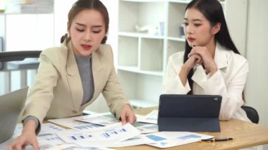 Genç Asyalı kadınların dizüstü bilgisayarları ve belgeleriyle bir araya gelerek proje mali raporları şirket işbirliği kavramını tartıştıkları bir iş toplantısı