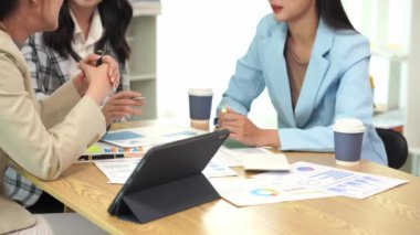 Genç Asyalı kadınların dizüstü bilgisayarları ve belgeleriyle bir araya gelerek proje mali raporları şirket işbirliği kavramını tartıştıkları bir iş toplantısı