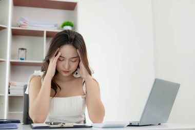 Yorgun ve fazla çalışan Asyalı kadın göz yorgunluğundan muzdarip, baş ağrılarından muzdarip gözlerini kapalı tutarak, finansal hataları düşünerek, çok fazla harcama yaparak..