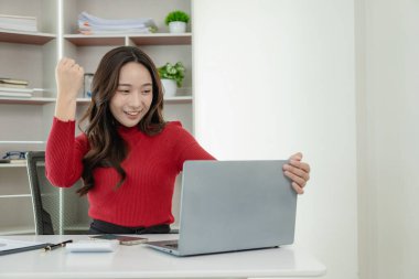 Genç Asyalı mutlu bir çalışan masada oturuyor ve bilgisayar ve hesap makinesiyle çalışıyor. Mali belgeler, hukuk şirketinin vergi oranlarını hesaplıyor..