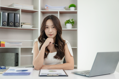 Genç Asyalı mutlu bir çalışan masada oturuyor ve bilgisayar ve hesap makinesiyle çalışıyor. Mali belgeler, hukuk şirketinin vergi oranlarını hesaplıyor..